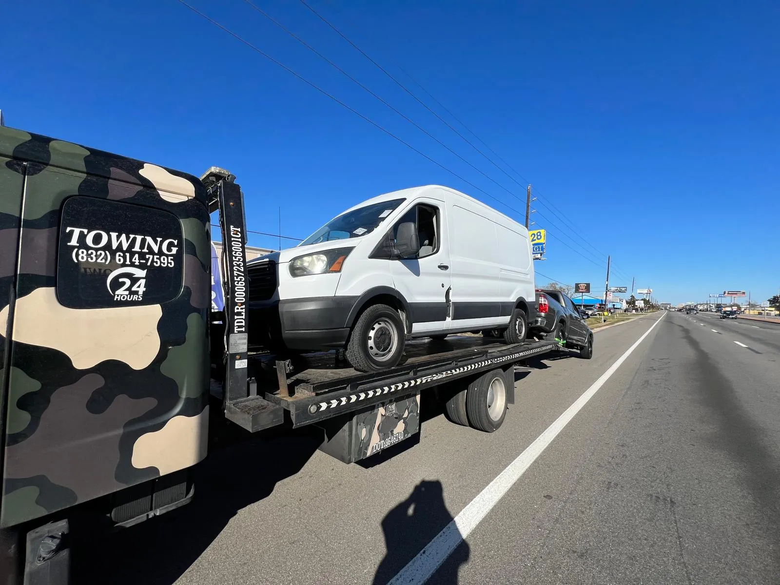 White Ford Transit cargo van on flatbed tow truck on Houston TX highway